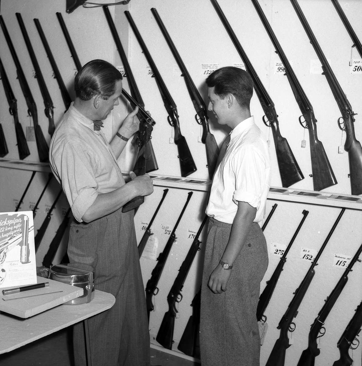 Två män tittar på jaktgevär i oidentifierad butik, sept 1951