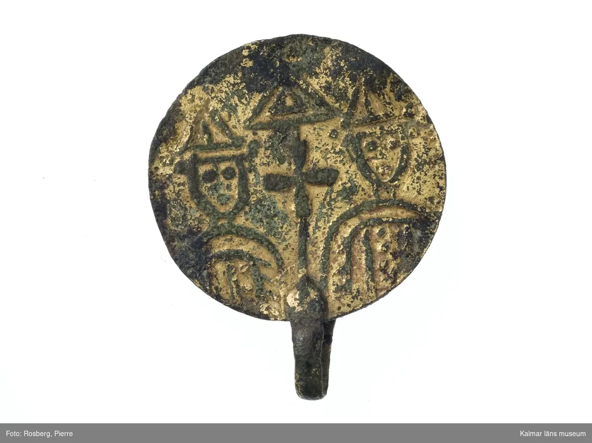 KLM 18916. Amulett, brakteat. Av brons med förgyllning, Rund. Motiv med två figurer i mitror, i mitten ett kors och över detta en gavelformig figur. Nedtill en ögla.