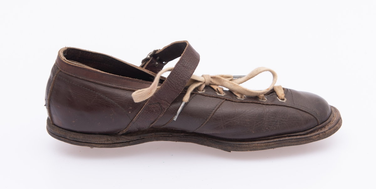 Ett par sko, produsert med tanke på bruk i orienteringsidrett. Skoene er sydd av brunt lær. Såla består av flere lag av forholdsvis tjukke lærtyper.  Yttersåla har en sliss langs ytterkantene av tå-, ball- og gelenkpartienes ytterkanter, der det er en søm som binder sålelærene sammen.  Jernstifter under hælpartiene typer på at en forsterkning er spikret fast der. Ellers er sammenføyinga av sålene forsterket med et par gjennomgående nagler under ballepartiene på begge skoene.  Sålene har metallpigger som skulle sikre løperen bedre feste på løpsunderlaget. Det er to slike pigger under hælene, to under ballene og to under tåpartiene.  Piggenes lengde er om lag 1 centimeter. Overlæret er forbundet med sålene ved hjelp av avsømmer langs skoenes ytterkanter.  Det er forsterket med ei tåhette som er trukket bakover langs ytterkantene på den spalta der skoene åpnes og snøres. Her har hver sko fem par lissehull omgitt av sekskantete metallmaljer.  Skolissene er av tekstilt materiale, men med 2 centimeter lange metallbeslag i endestykkene.  Under spalta med snøring er det vristlapper av tynt, brunt lær. Ellers har skoene vristreimer, der endeflatene er sydd fast til overlærets utside i skrå vinkel i forkant av hælkappene.  Vristreimene strammes i nålespenner i enden av de reimene som sitter på yttersida av overlæret.