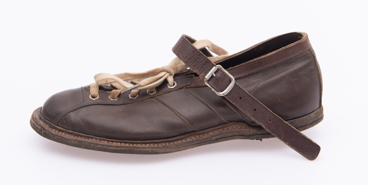 Ett par sko, produsert med tanke på bruk i orienteringsidrett. Skoene er sydd av brunt lær. Såla består av flere lag av forholdsvis tjukke lærtyper.  Yttersåla har en sliss langs ytterkantene av tå-, ball- og gelenkpartienes ytterkanter, der det er en søm som binder sålelærene sammen.  Jernstifter under hælpartiene typer på at en forsterkning er spikret fast der. Ellers er sammenføyinga av sålene forsterket med et par gjennomgående nagler under ballepartiene på begge skoene.  Sålene har metallpigger som skulle sikre løperen bedre feste på løpsunderlaget. Det er to slike pigger under hælene, to under ballene og to under tåpartiene.  Piggenes lengde er om lag 1 centimeter. Overlæret er forbundet med sålene ved hjelp av avsømmer langs skoenes ytterkanter.  Det er forsterket med ei tåhette som er trukket bakover langs ytterkantene på den spalta der skoene åpnes og snøres. Her har hver sko fem par lissehull omgitt av sekskantete metallmaljer.  Skolissene er av tekstilt materiale, men med 2 centimeter lange metallbeslag i endestykkene.  Under spalta med snøring er det vristlapper av tynt, brunt lær. Ellers har skoene vristreimer, der endeflatene er sydd fast til overlærets utside i skrå vinkel i forkant av hælkappene.  Vristreimene strammes i nålespenner i enden av de reimene som sitter på yttersida av overlæret.