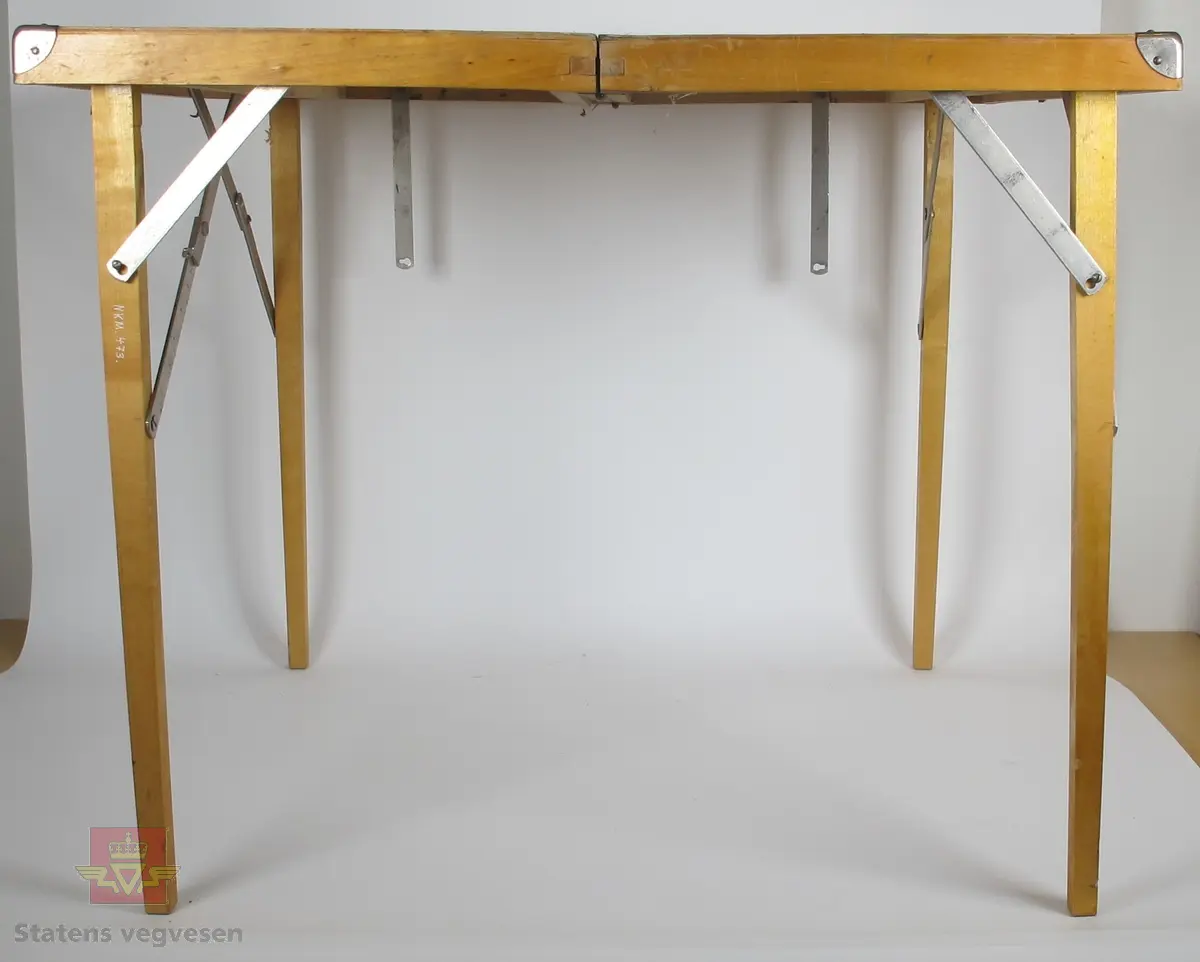 Sammenleggbart bord med 4 tilhørende stoler. Bordet er hovedsaklig laget av tre og har 2 bein i hver ende av bordet som skyves opp ved hjelp av en metall brakett. På midten av bordet er det 2 hengsler som holder de 2 bordplatene sammen og får det til å bli sammenleggbart. Når bordet er sammenlagt er det et håndtak av lær for å bære det hele og to metall hengsler for å forhindre at det åpner seg. Klappstolene som medfølger er hovedsaklig laget av metall og tekstil, og passer i rommet som oppstår når bordet lukkes.