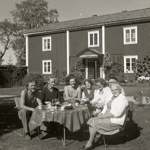 Hilding(med bar överkropp) och Adéle(till höger om honom i bild) med gäster sitter ute i solen vid ett dukat kaffebord, Sunnanåker 1986.