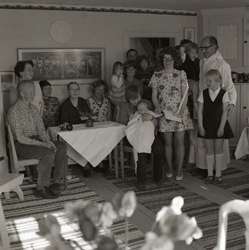 Lill-Annas dop sommaren 1973, här i ett rum på gården Sunnanåker. Alla vuxna och barn har samlats runt ett bord för en gruppbild.