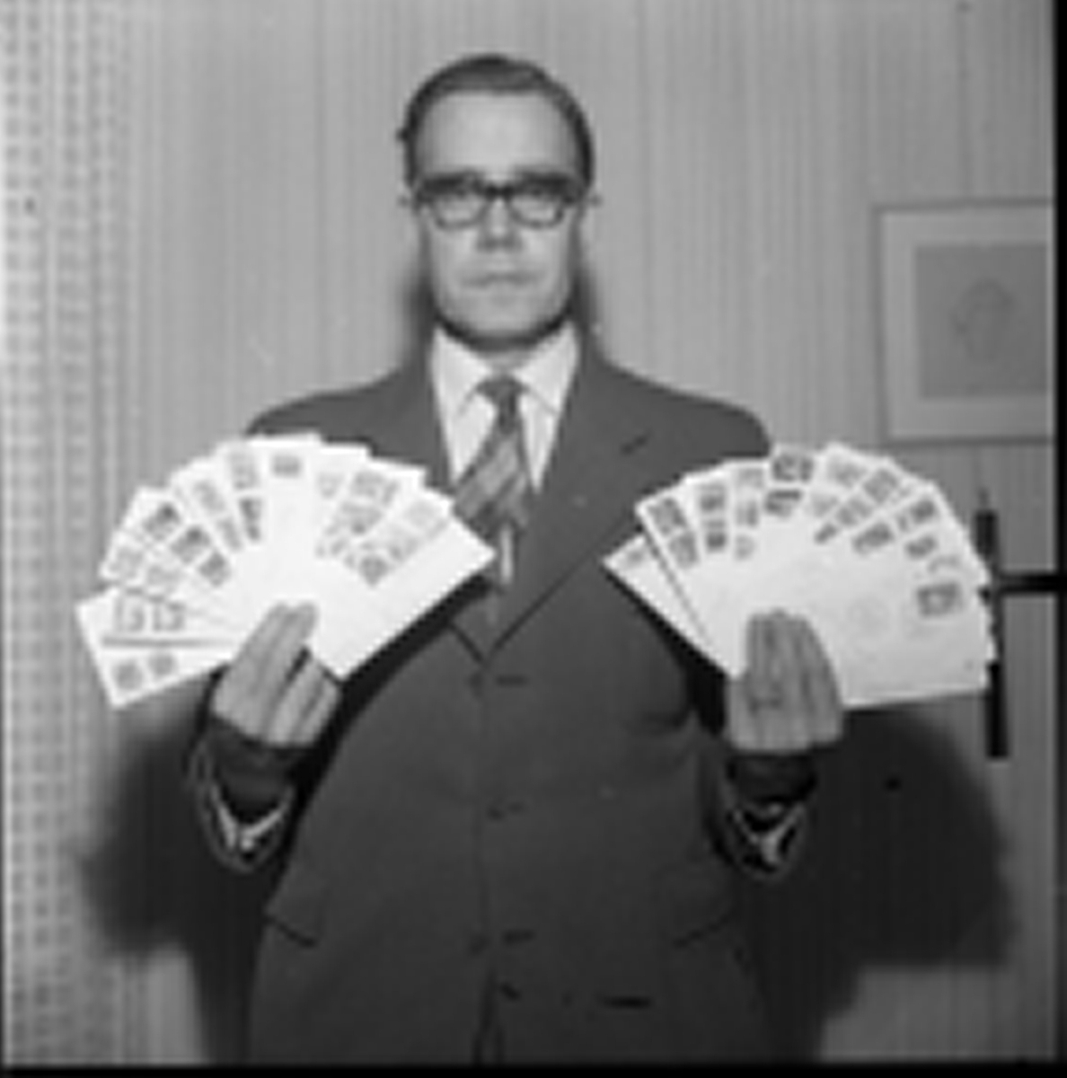 En herre står med flera kuvert i händerna. Han håller dem som solfjädrar eventuellt för att visa upp frimärkena klistrade på kuverten.