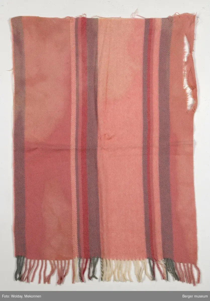 En pleddprøve i stripemønster. Prøven har klippekant på tre av sidene. Mønsteret karakterisereres av 14 langsgående felt og striper i forskjellge farger. Fargene i duse rosatoner.