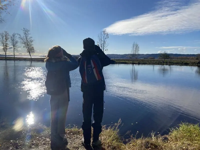 Foto av to barn som kikker i hver sin kikkert ute i naturen ved vannet