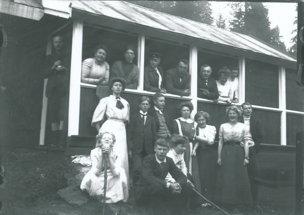 Medlemmer og venner av familiene Rydgren og Berger utflukt til hytte. Granskog i bakgrunnen.