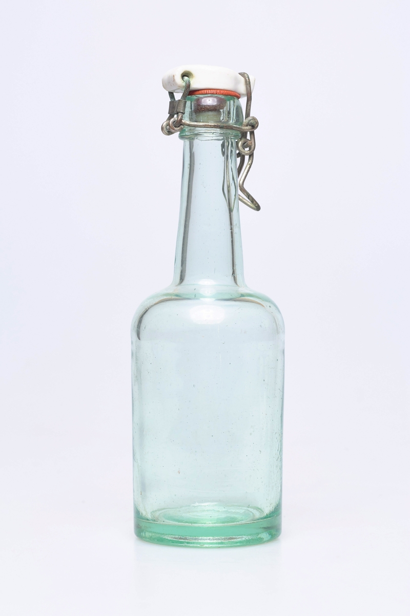 Glassflaske av klart glass med noe grønnskjær. Har hvit plastkork med metallfeste.