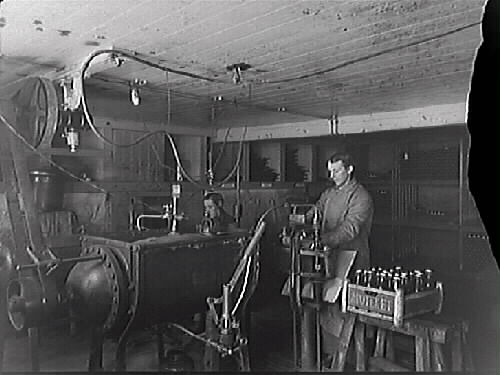 Apoteket Kronans vattenfabrik, Varberg. Alfred Petersson och John Nilsson står vid apparaterna i källaren.
(Fotografiet är skadat i högerkanten)