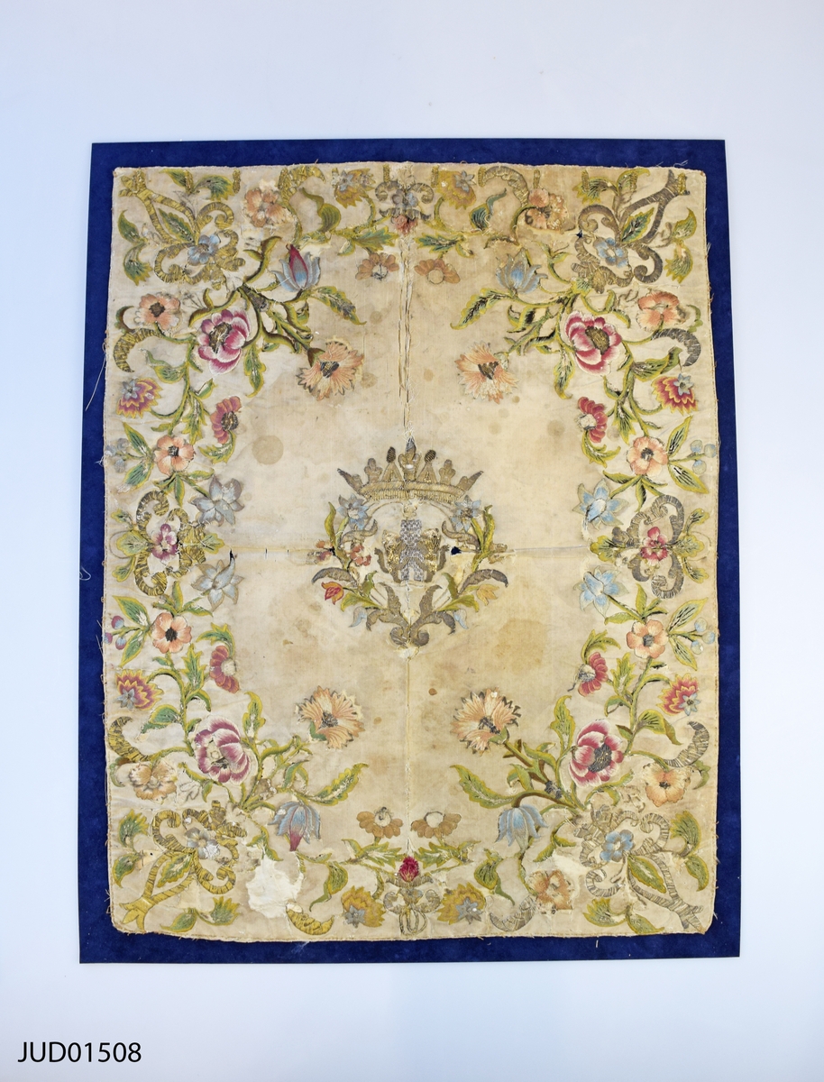 Textil i sidenbrokad med blommönster på vit botten. Två lejon i mitten med en krona ovan.
Är möjligen Torahförhänge med ursprung i Italien.