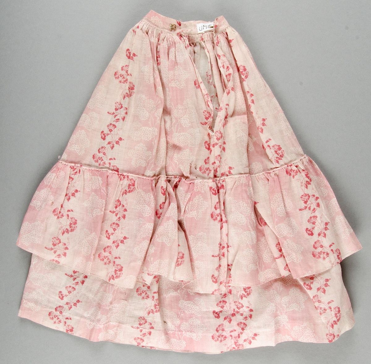 Blus och kjol av rosa- och vitrandig bomullsvoile med tryckt mönster i rött och rosa på vit botten. Livet kantat med röda ylleband.