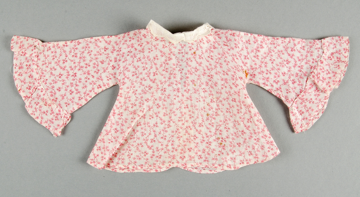 Dockklänning, blus och kjol av tunt tuskaftat bomullstyg s.k. kattun med rosa mönster på vit botten. Liten vit brodyrkrage.