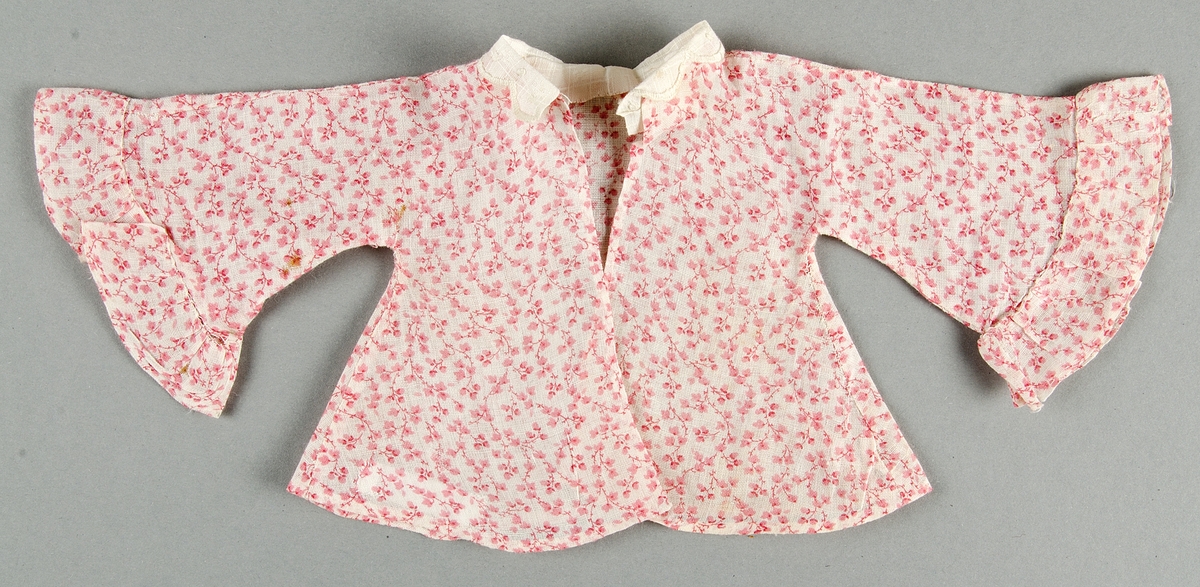 Dockklänning, blus och kjol av tunt tuskaftat bomullstyg s.k. kattun med rosa mönster på vit botten. Liten vit brodyrkrage.