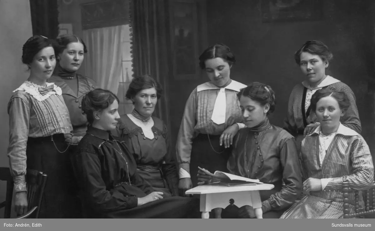 Gruppbild med åtta yngre kvinnor i inomhusmiljö. På bildens baksida står: 8 st. gamjäntor. Sittande längst till höger är Märta Nordlander (Mårtes-Märta). Ur en samling som tillhört Olof Mattsson, Gräfte, Stöde.