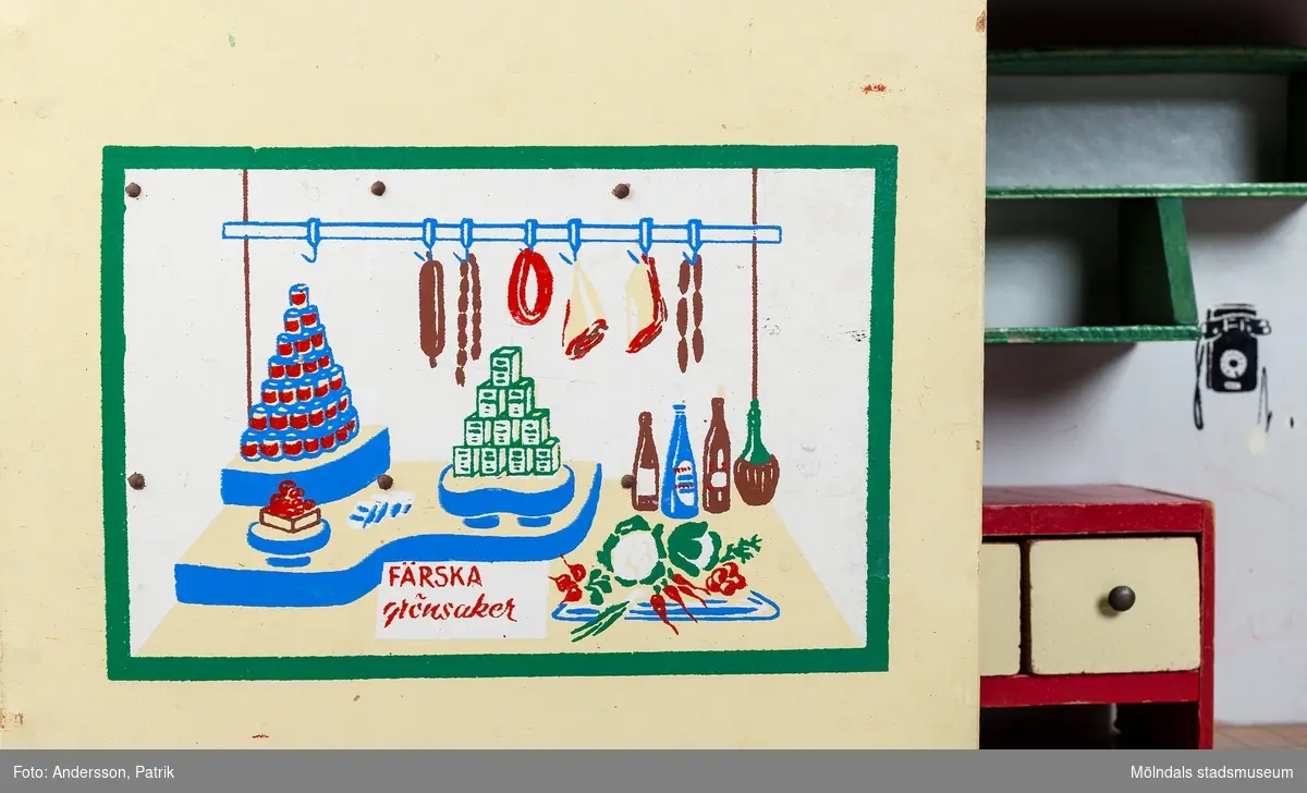 Leksak i trä i form av en liten affär. På framsidan finns texten "Kährs Diversehandel", dekor i form av två skyltfönster och en liten dörr med ett handtag i metall. Fronten består av två luckor går att öppna. Inuti finns en butiksinredning med gröna hyllor och en lös röd butiksdisk med sex gula utdragbara lådor.
Allt är tillverkat i trä. Affärens utsida är målad i en ljusgul färg, med ett tak som är bemålat med tegelröda tegelpannor. Under takåsen löper en röd list med texten "Kährs Diversehandel" målat med vita bokstäver.
Leksaksbutiken är tillverkad av Kährs. Företaget grundades 1857 och tillverkade till en början leksaker och möbler, men tillverkningen övergick efter andra världskriget alltmer till att omfatta endast dörrar och golv.