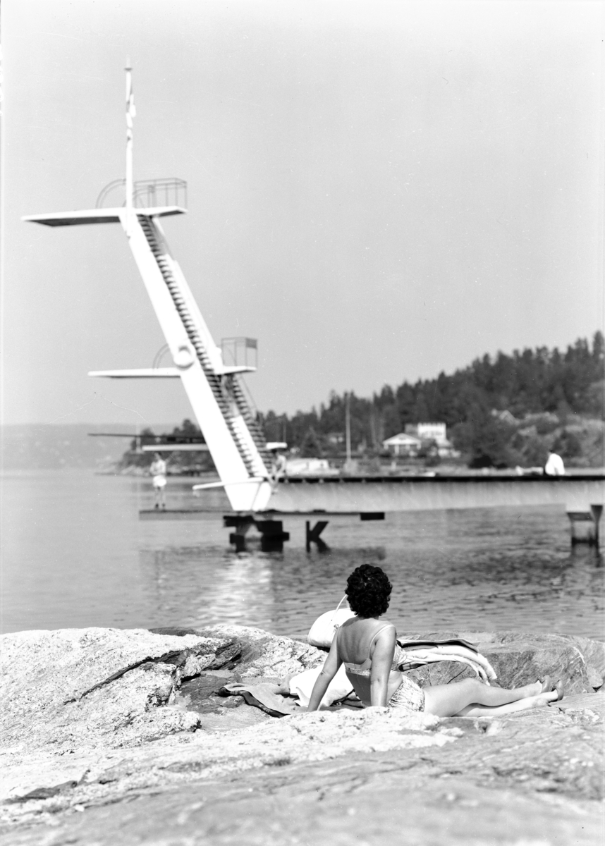 Svarthvittbilde av stupetårnet på Ingierstrand bad med en kvinnelig badegjest i forgrunnen. Anlegget sto ferdig i 1934.