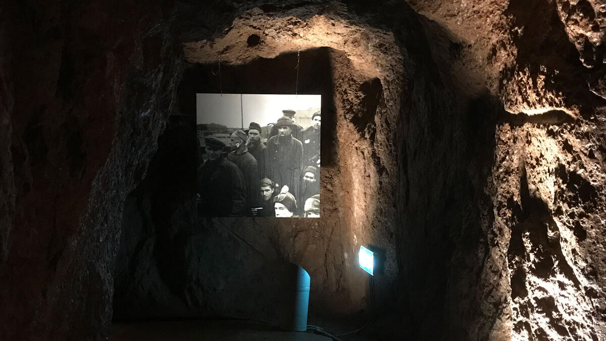 Vi ser et sort-hvit-fotografi som henger på en ruglete steinvegg i et mørkt rom, det vil si inne i en hule.