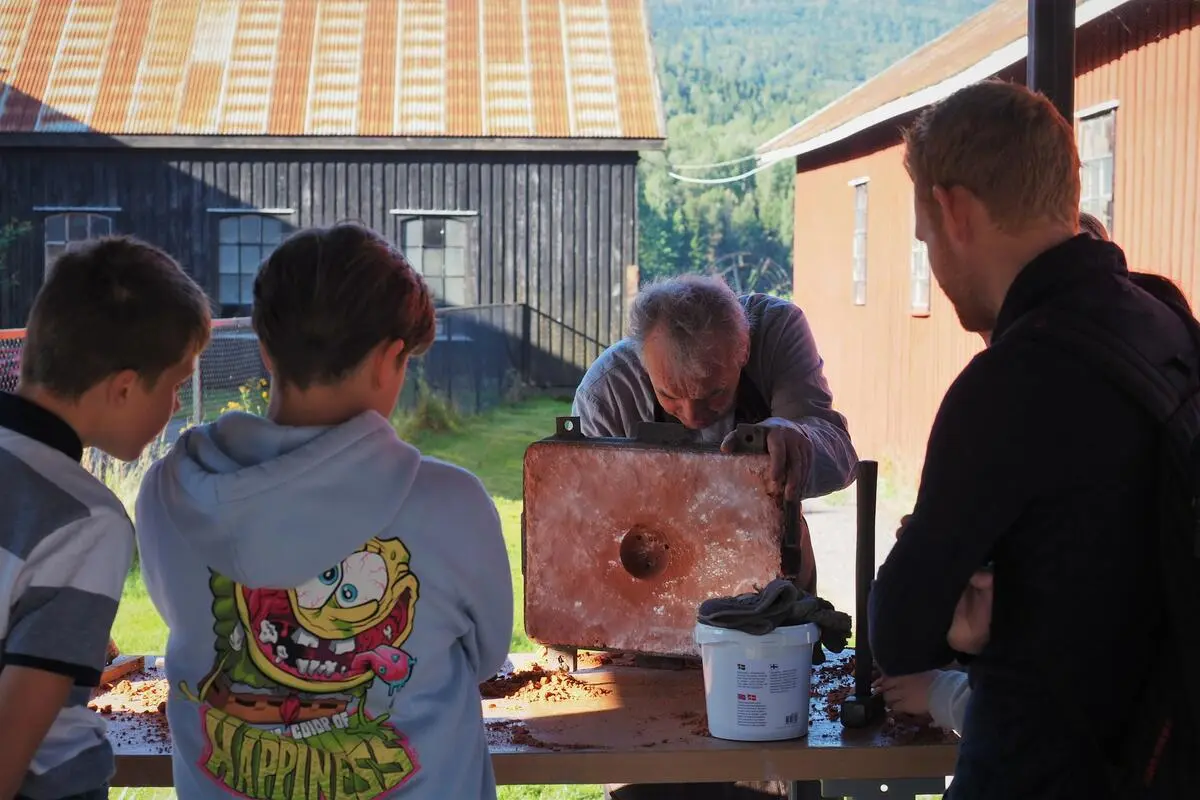 Vi ser ryggene på noen barn som ser på en mann som holder på med noe ved et bord