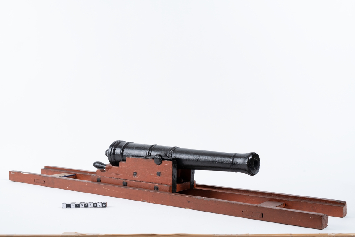 Kanonmodell: galérlåda med släde, beslagen, samt kanon. Lavetten av trä, rödmålad. Kanonen av järn, svartmålad. Tillbehör: 1 st ställhult. Lavetten L = 955 mm B = 142 mm H = 130 mm.