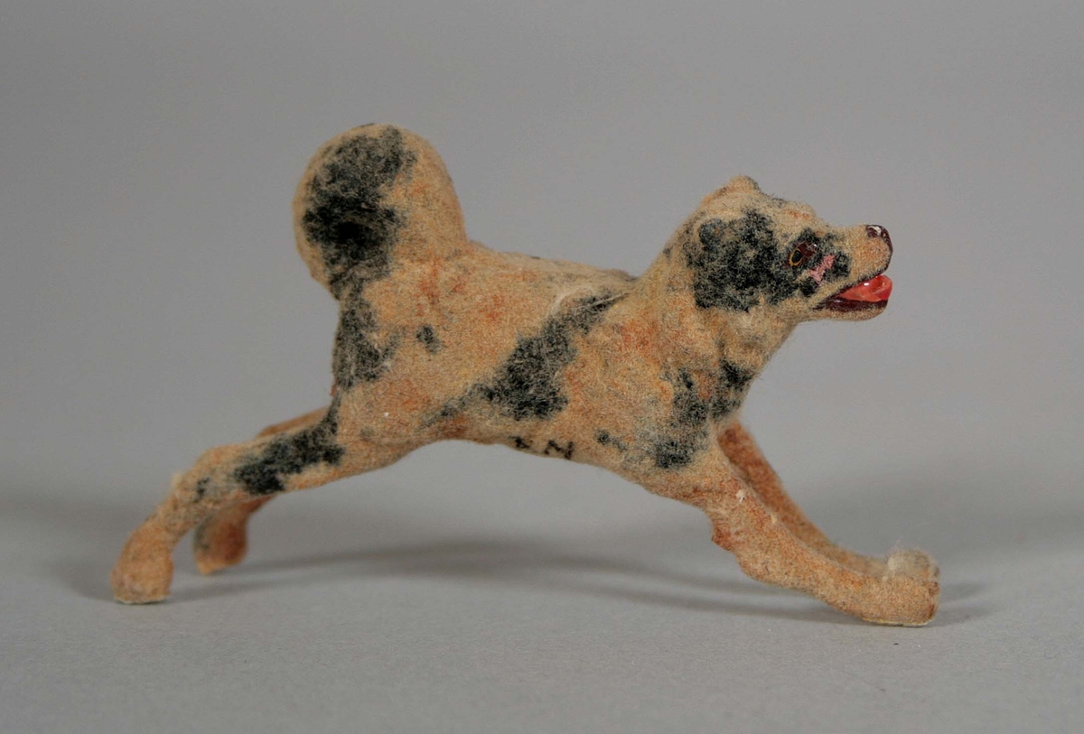 Hund i springande ställning i gips. Överdragen med pälslikande ytskikt och målad i ljusbrunt och svart.