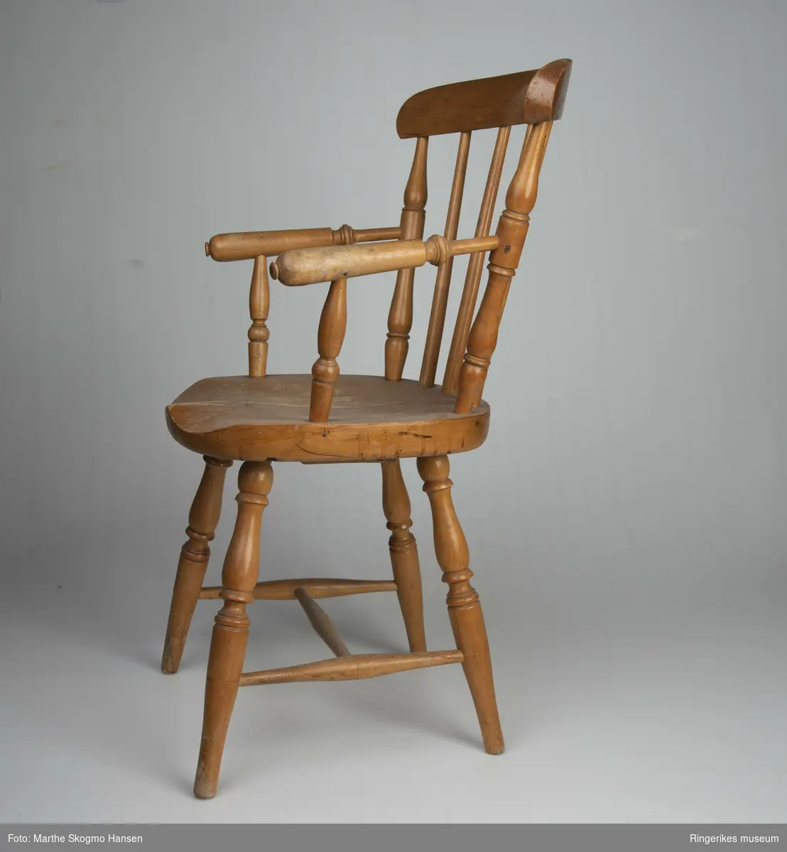 Barnestol med armlener, pinnestol. Stolen er profesjonelt laget. Alle beina er dreid med fint mønster, og mellom beina er det tre sarger i H-form. Ryggbrettet blir holdt oppe av 6 pinner og er ca. 5 cm bredt. De to ytterste pinnene er dreid i fin profil. Det er også armlenene. Ytterst på armlenene er det dreid en liten knapp. Knappen på høyre side er litt ødelagt. Setet har en fin sitteprofil. Stolen er lakkert. Lakken er slitt på setet og armlenene, og nederst på føttene. Sargene har også slitasjespor. Det er to sprekker i setet, og under er det skrudd på en trekloss, muligens for å stabilisere det.