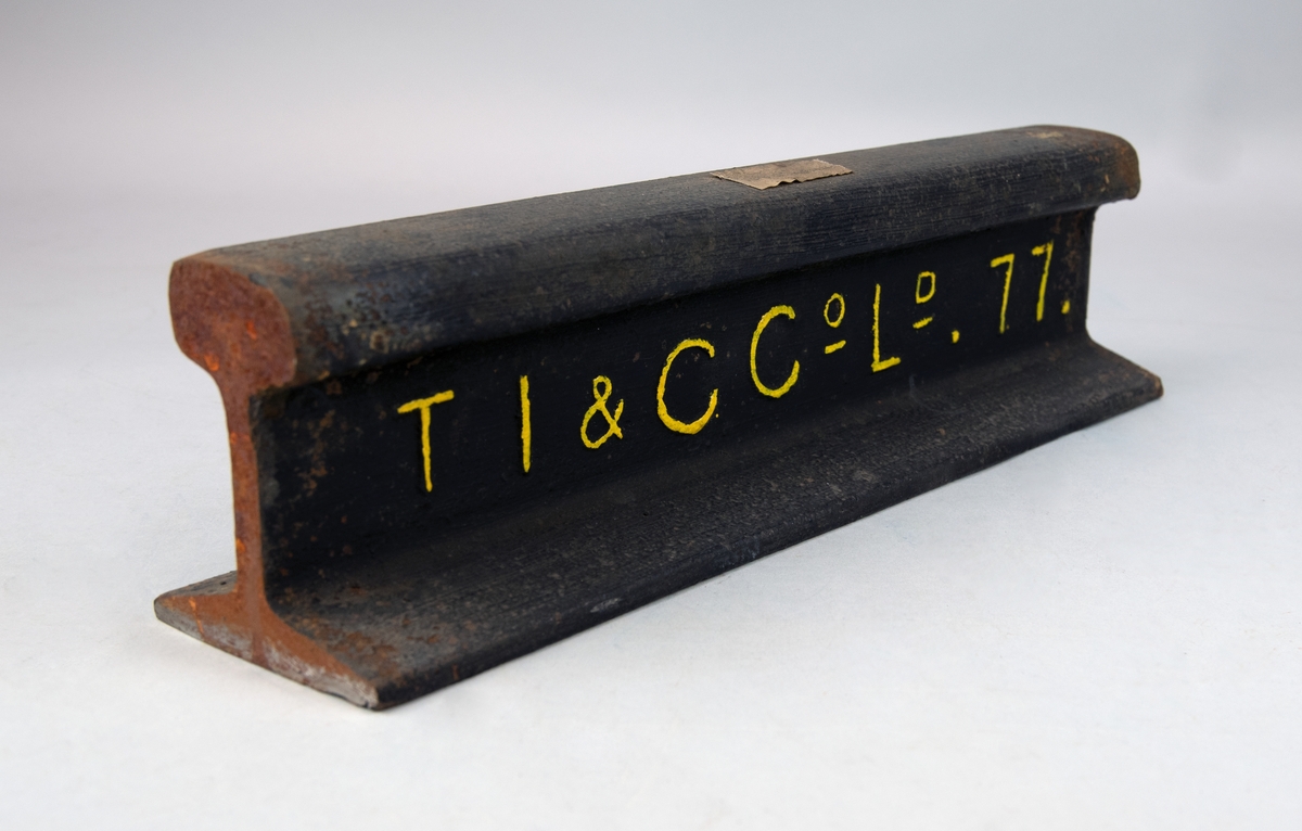 Vingnolräl av järn med huvud, liv och flatbottnad fot. På ena långsidan står det "TI & CCoLd . 77.", senare målad med gul färg. Tejpbit på ovansidan där det står "Vikt 1[möjligen 4] kg/meter".