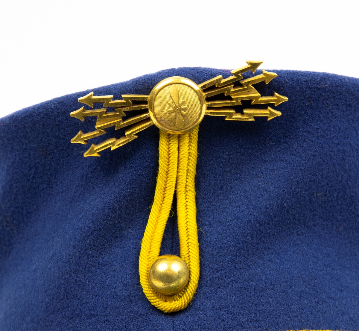 Mössa m/23, med fälttelegrafkårens flygkompanimärke m/16. Mössan har gul passpoal och läderband, hög rak blå kulle. Emblem i form av en knapp med propeller omgiven av gnistor. Bild av mössan utanpå kartongen.