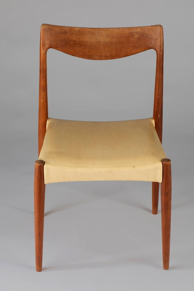 Stol i eik med sete i lys naturfarget møbelhud. Stolen har runde ben som smalner nedover. Åpen rygg med buet toppstykke.