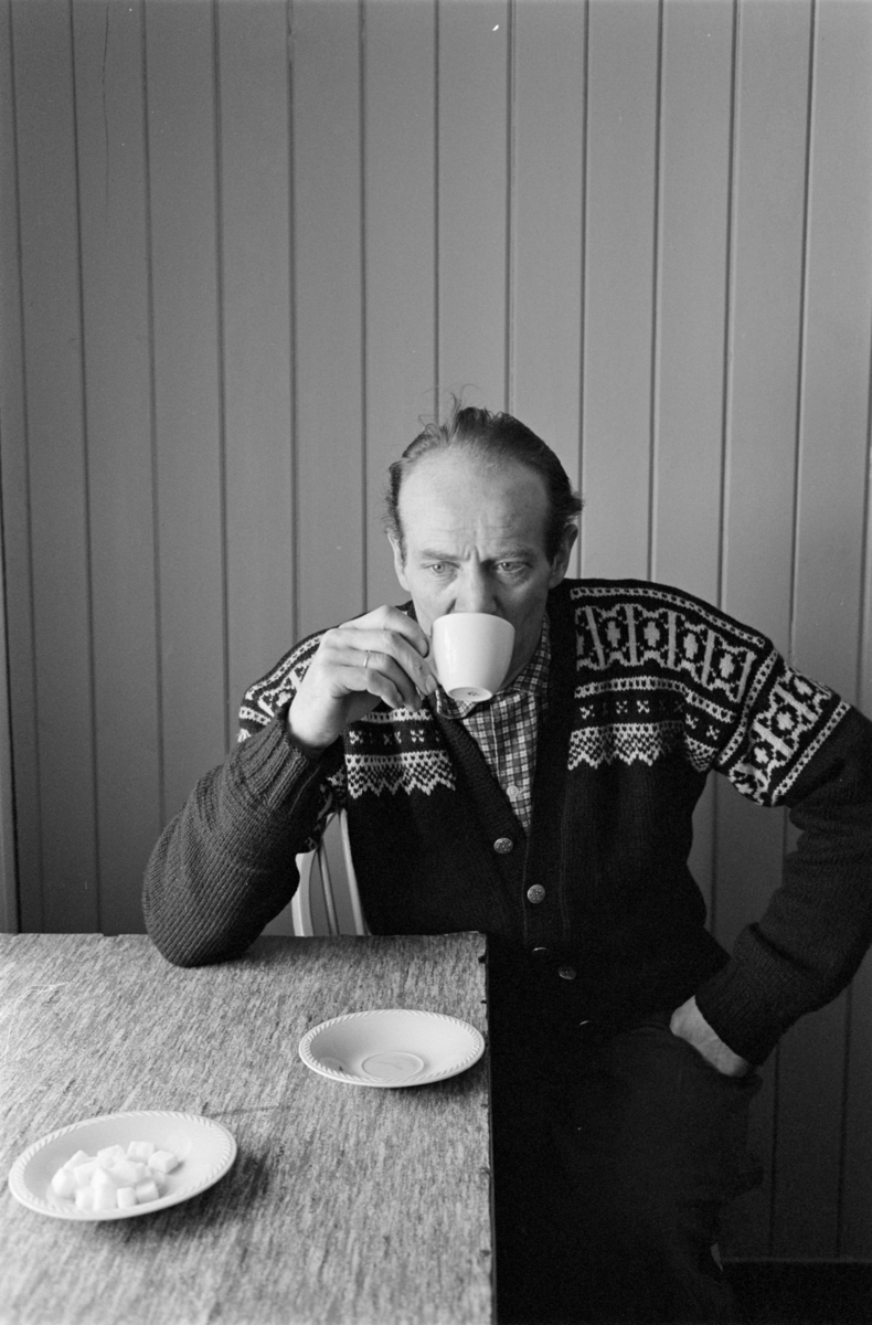 En mann sitter ved et bord og drikker kaffe.