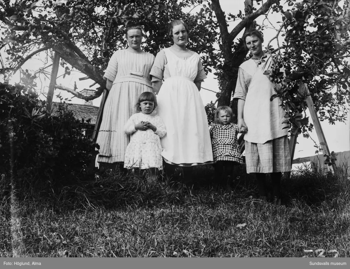 Tre kvinnor och två små barn i trädgården.