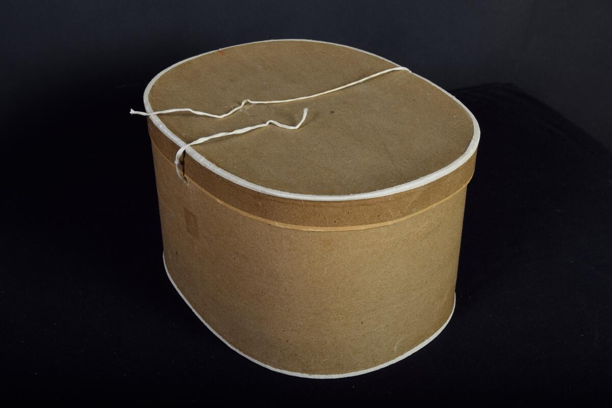 Hattask, förvaringsask med lock av brun papp med knytband. Troligen inköpt i Umeå. 