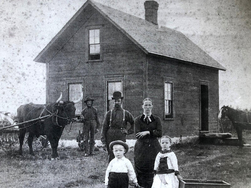 Mor og far med to barn utenfor huset sitt anno 1880