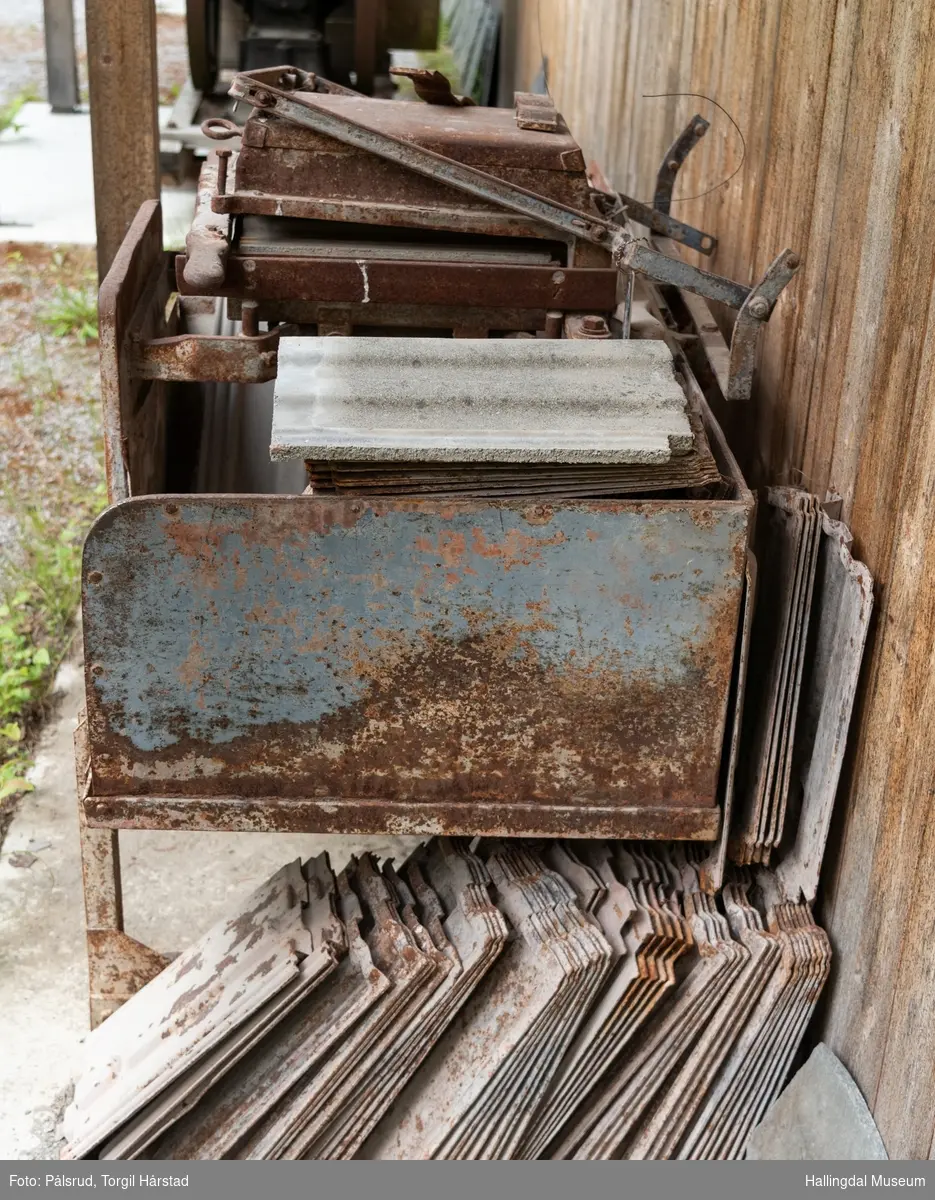 Taksteinspresse i støpt jern med takstein og støpeformer. Til å presse (støpe) takstein. Har vært i bruk på gården Østenfor, Nesbyen.