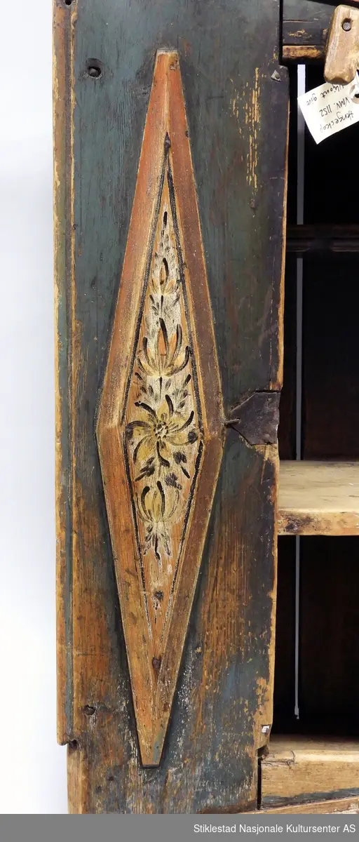 Hengeskapet dekorert med rose- og figurmaling av «rokokkomaleren» Ole Haldosen Berg (1747-1828). Skapet er i bondestil med ei dør i front. Malte speiltfelt. Skapet har liggende profiler i forskjøvet rektangel, disse er dekorert med malt blomsterdekor (hevet over skapets overflate). Over og under dør er profilene montert horisontale, vertikale på høyre og venstre side av dør. Speilfeltet på dør er dekorert med figurmaling, mann og dame i rokokkoklær. Over døra er det montert en vrider i tre, dette for å holde døra lukket. Døra har originale hengsler, nøkkelbeslag mangler, løs låskasse. Grunnfargen er blå. Innvendig har skapet to hyller. 
Gesimsen øverst på sideveggene er fjernet, og spikrene på hengslene er skiftet ut, ellers er skapet intakt med originale beslag (festet på nytt?).