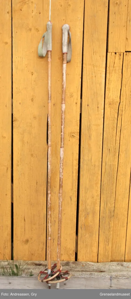 Et par skistaver av bambus med håndtak og stropper i hvitt skinn, pyntet med en tynn bise i rødt skinn. Trinser av bambus og rødt skinn, tupp av lettmetall og jern.