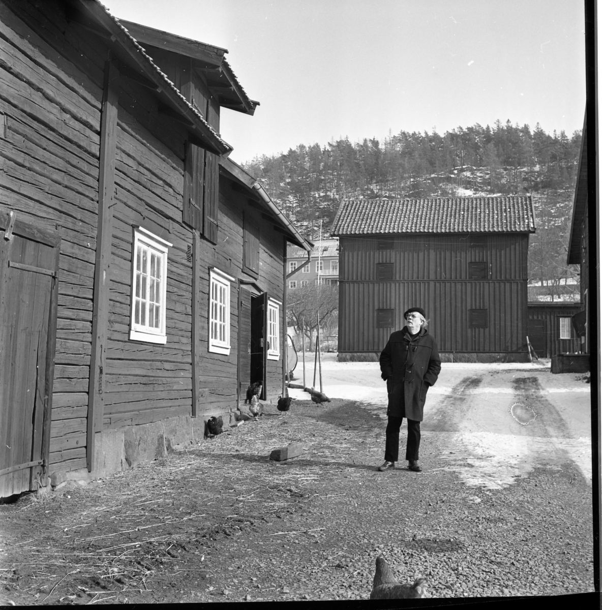 En man med basker och rock står på gårdsplan till Gränna prästgårds ekonomibyggnader. Till vänster stall och i bakgrunden en magasinsbyggnad.