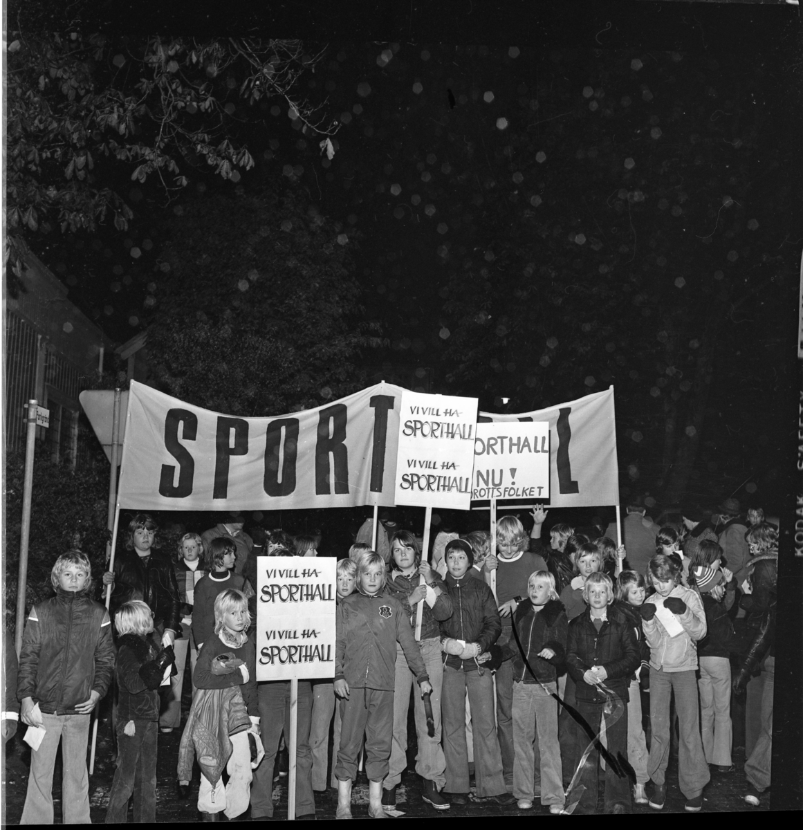 Ungdomar med banderoll och plakat om "Sporthall". Grännabor demonstrerar för att få en sporthall till Gränna. Det är oktober och mörkt.