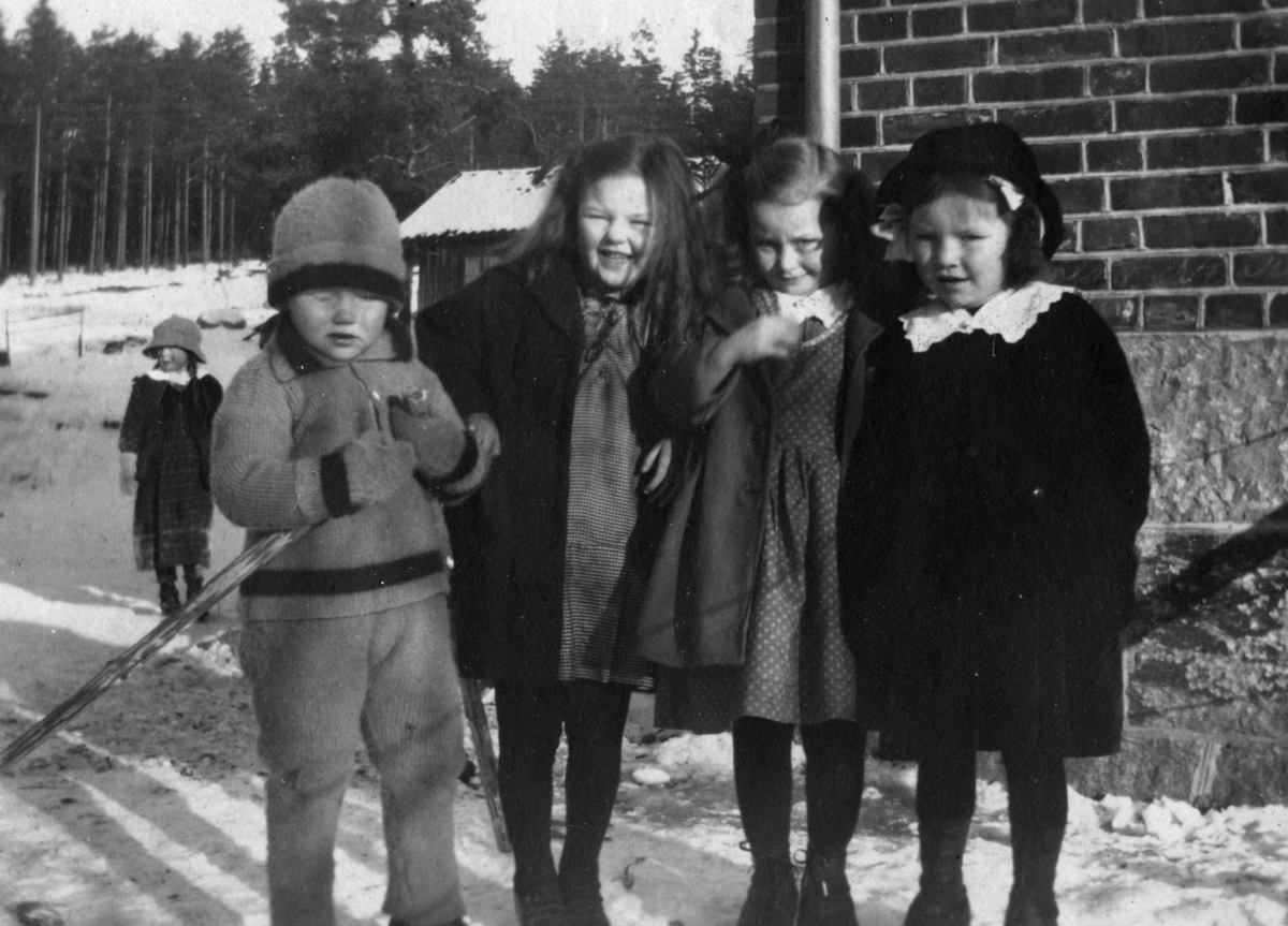 Fem barn utanfor eit hus på vinteren
