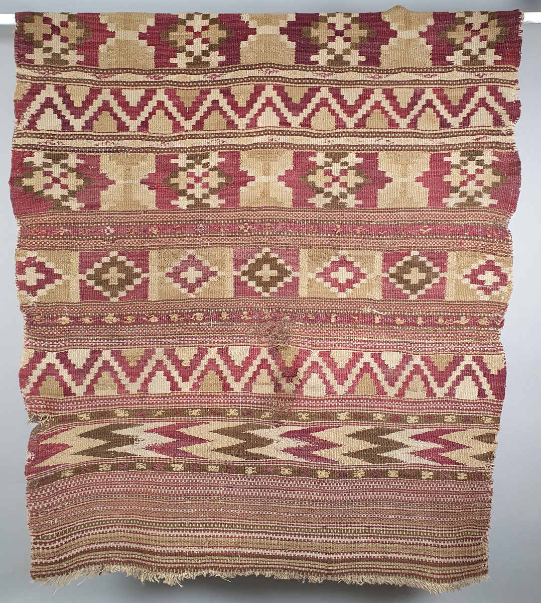 Åkle med ulike geometriske mønstre i striper burgunder-rødt, grønt og beige. Renning av lin, innslag av ull.