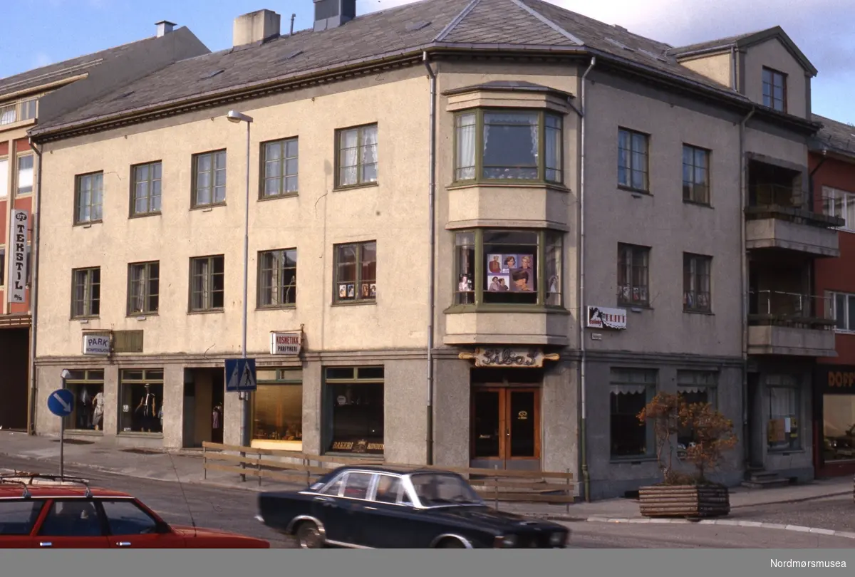 På hjørnet Langveien/Skolegata på Kirkelandet i Kristiansund, med bakeriet til Sibas. Datering er ikke kjent, men muligens på 1980-tallet. Fra Stein Magne Bach sin private fotosamling. Denne samlingen består av dias fra perioden omkring 1980. Fra Nordmøre museums fotosamlinger.