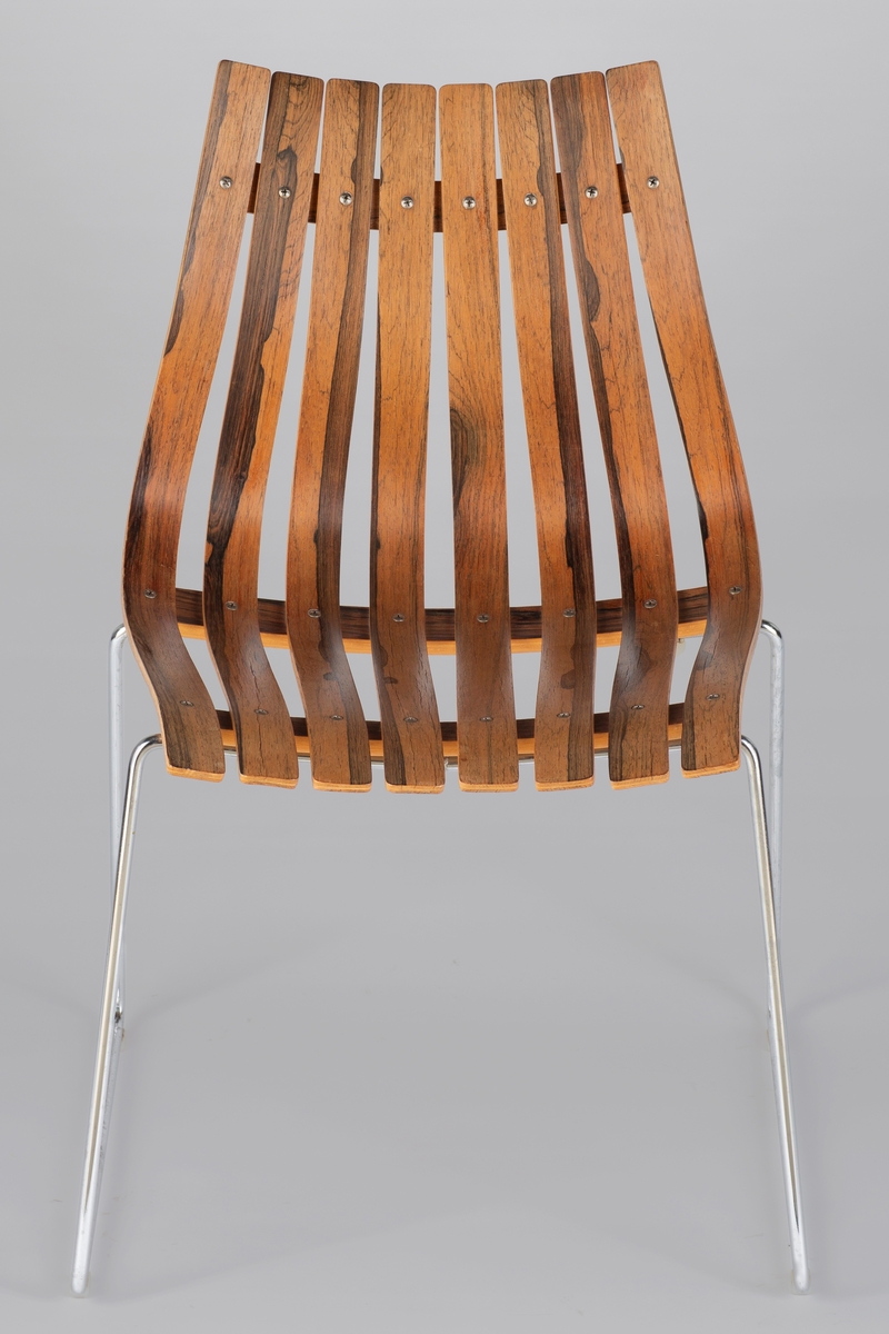 Stolen består av åtte langsgående, buede staver i laminert bøk finert med palisander, samlet med to horisontale treforbindelser under setet og ett bak ryggen. Understell i forkrommet metall. Kan stables.