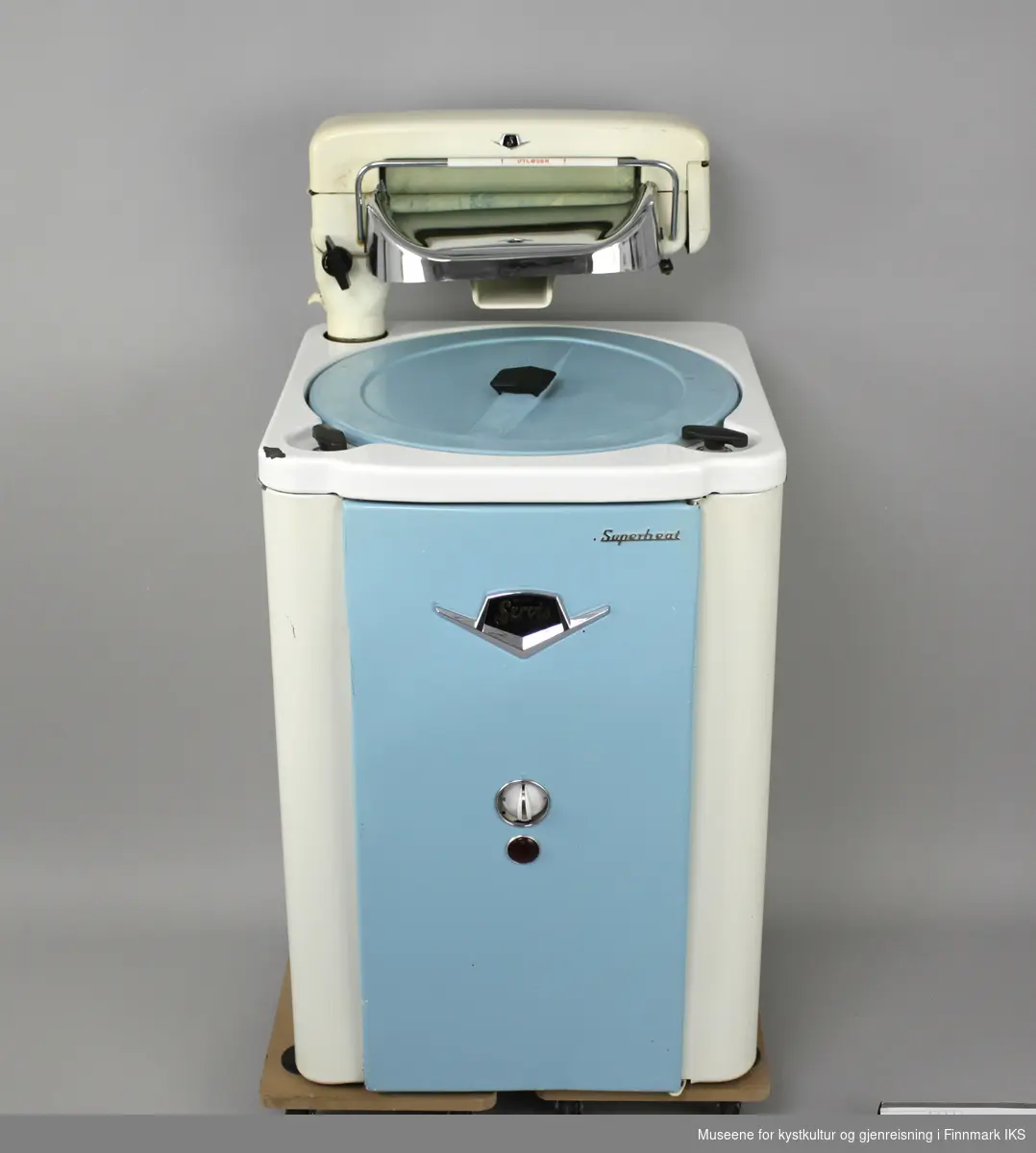 Denne vaskemaskinen er av emaljert metall, har avrundede kanter og en frontdør og lokk i blå lakkert metall. Maskinen har en bryter og en driftslys foran. 
Maskinen har en tilhørende elektrisk vrider (GMH.00891) som er festet på toppen. Vaskemaskinen er en såkalt "Agitatormaskin". Det betyr at den har en skovl i bunnen som beveger seg frem og tilbake i vaskeprosessen. Maskinen har et varmeelement og en elektrisk vannpumpe, samt fire hjul under. Hjulene er ikke montert. 
Oppå maskinen er en hendel som er merket: PUMPE PÅ-AV og hendel merket: TREKK OPP FOR START VASK. Den hvite bryteren foran er merket: I, II og III. På hjulene står det: FLEXELLO/MADE IN ENGLAND. Bak på døra er det skilt med følgende påskrifter: MÅ BARE TILKOBLES JORDINGSKONTAKT / 16 M 195299 MANUFACTURED BY WILKIN & MITCHELL LTD/ DARLASTON.S.SAFF. ENGLAND / Type E Volt 220. 
Med maskinen følger det en bruksanvisning, en vaskeklype (GMH.000894) og en gummislange (GMH.000893). Pakningen er porøs og det er 5 deler avbrudd som følger med separat.