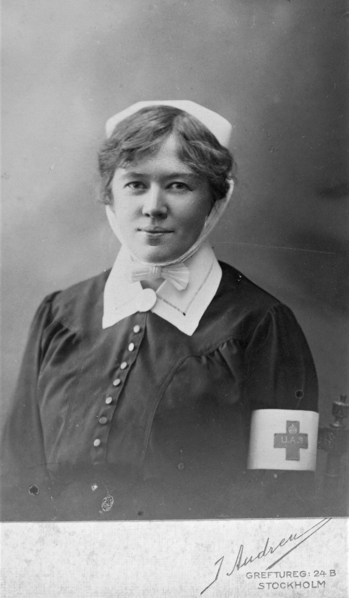 Ateljéporträtt av Hildur Selvén iklädd Röda Kors-uniform, taget i Stockholm. På armbindelns kors står det "U.A.S".