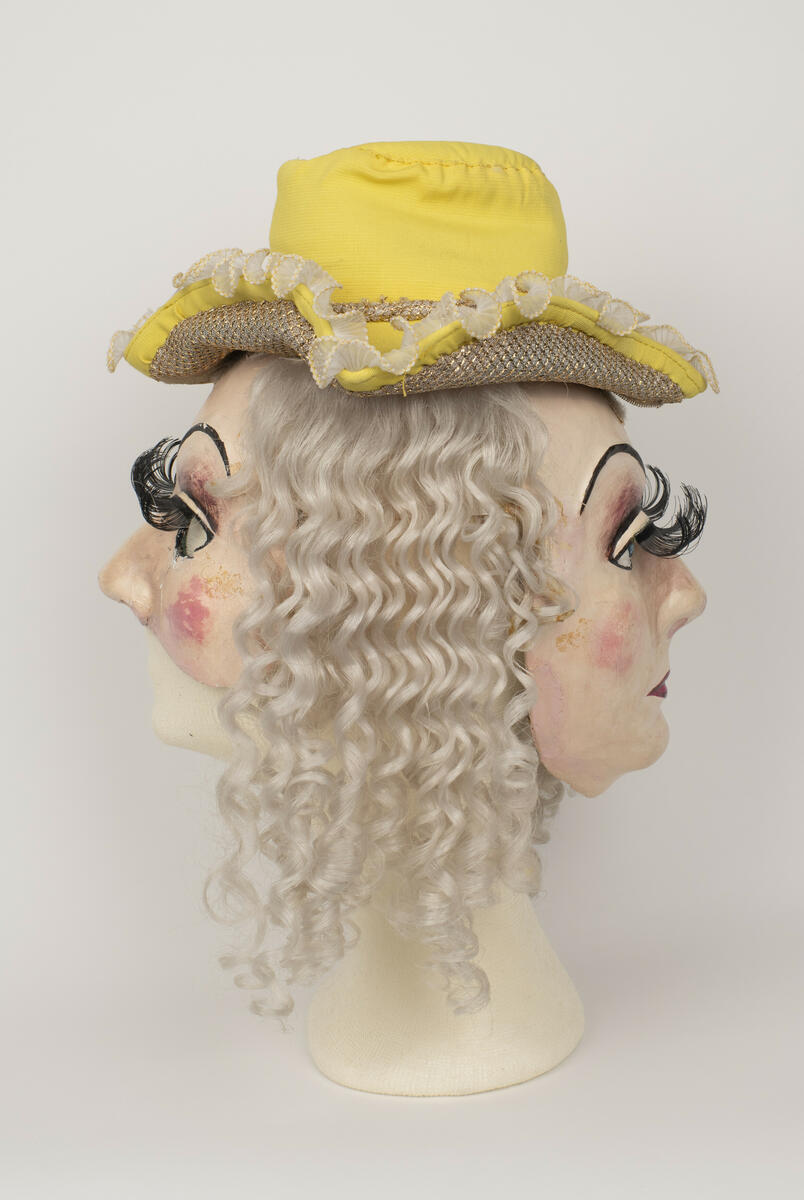 Dubbelmask med hatt och hår använd för rollen "Baronessan" i uppsättningen ”Pierrot i parken”.
Masken består av en halvmask som bärs över ansiktet och en ansiktsmask som bärs över bakhuvudet. Hatten och håret sitter fast i masken.