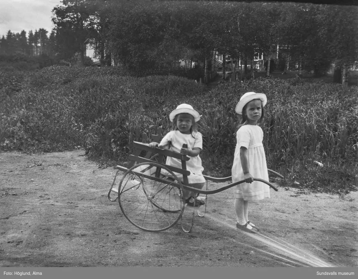 Två finklädda små flickor med en dragvagn.