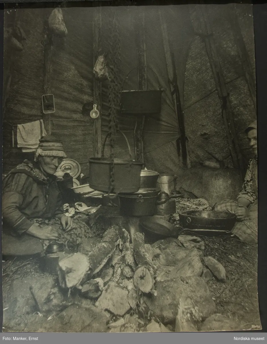 Kåtainteriör från Teukkajärvi, Tuolpukka. Kåtan tillhör änkan Inger Sevä som på bilden sitter vid en gryta. L.A. 1308. Jämför NMA.0073181.