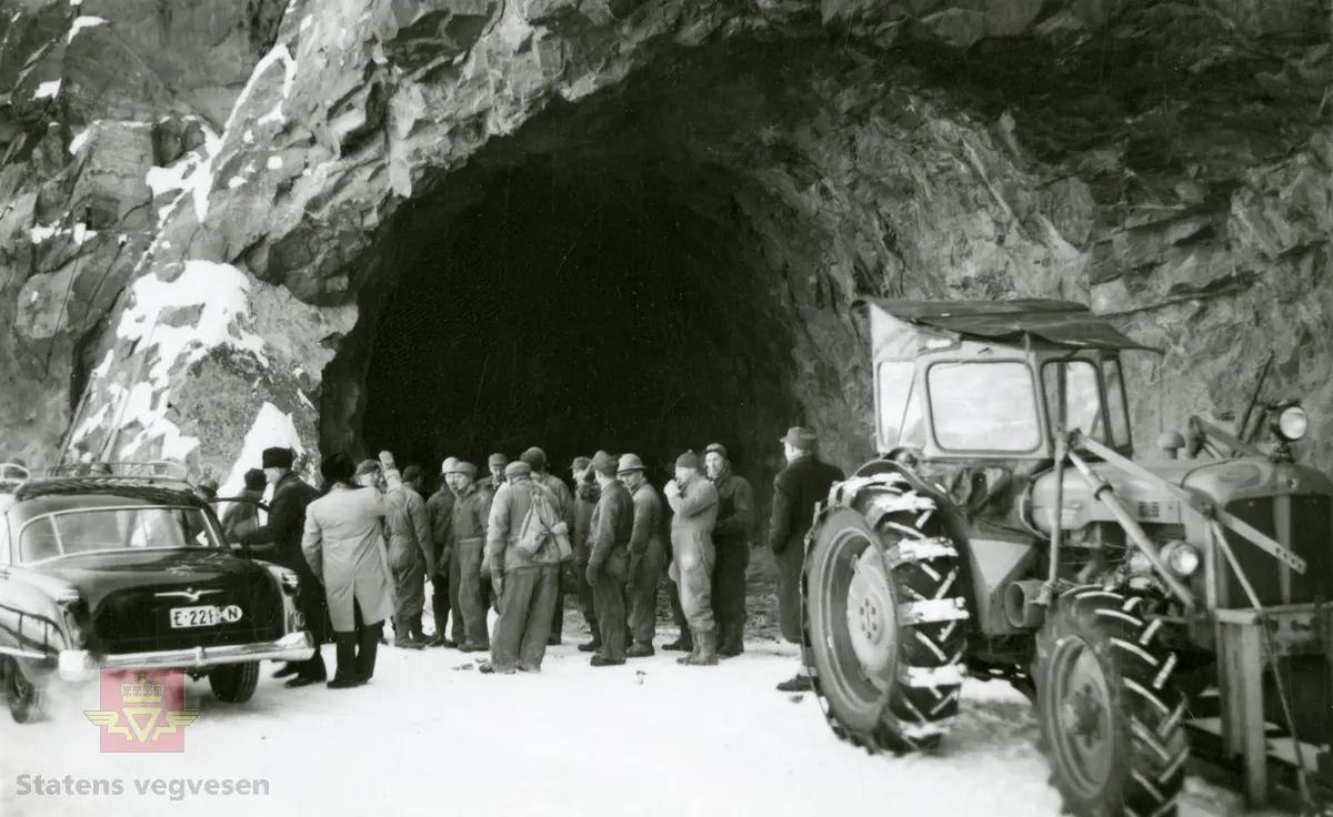 Tunnelarbeid i Kvamskleiva 1956-1957. Trolig er ingeniører på befaring og ser på arbeidet som utføres. 
Opel Kaptein (Kapitän på originalspråket) årsmodell 1954-1955. 
En Fordson Major firehjulstrekk med snøkjetting/plater som brukes i arbeidet.