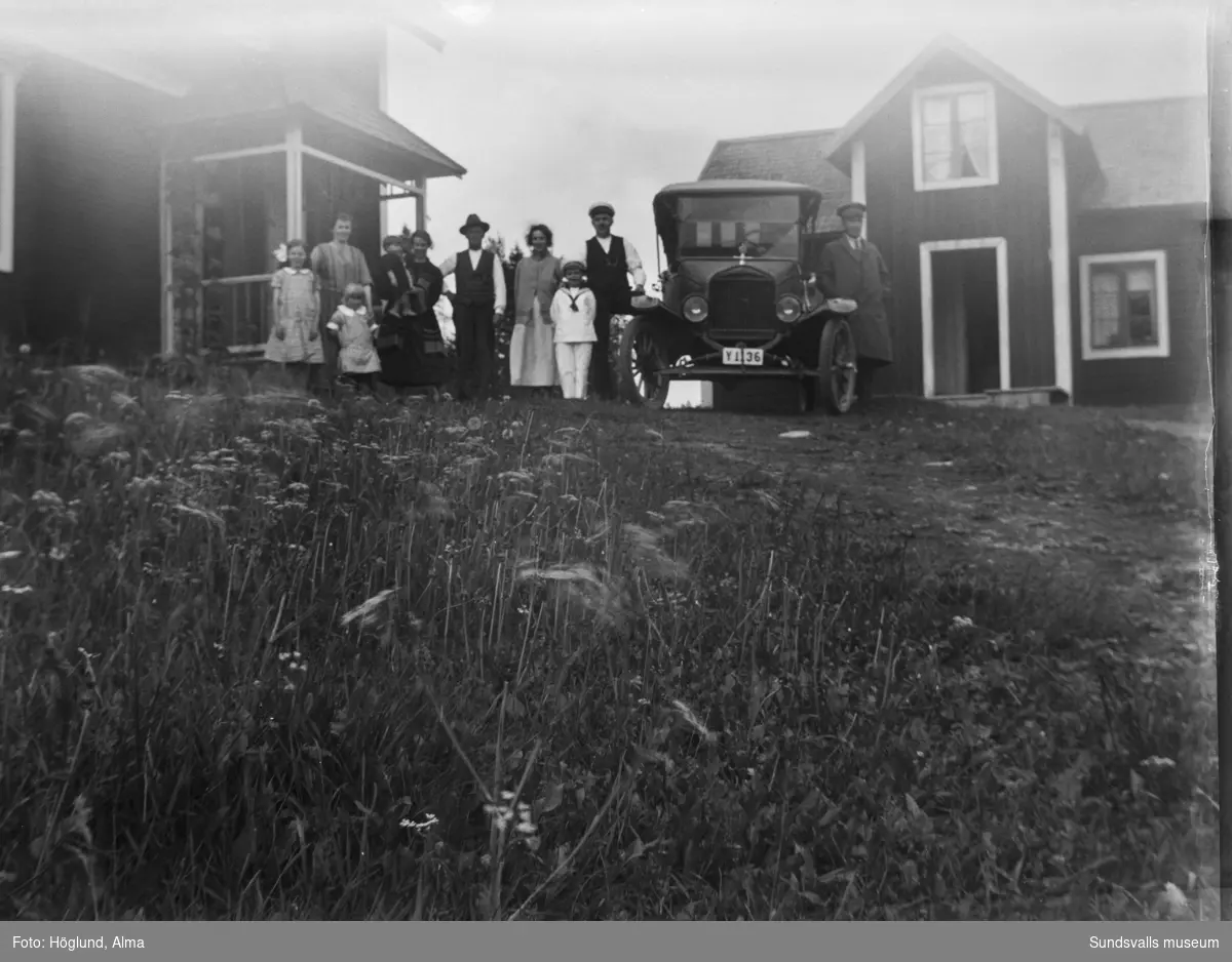 Familj/släkt samlade på gårdstunet med två bostadshus i vinkel. Intill står Gottfrid Höglunds T-Ford 1922 samt chaufför.