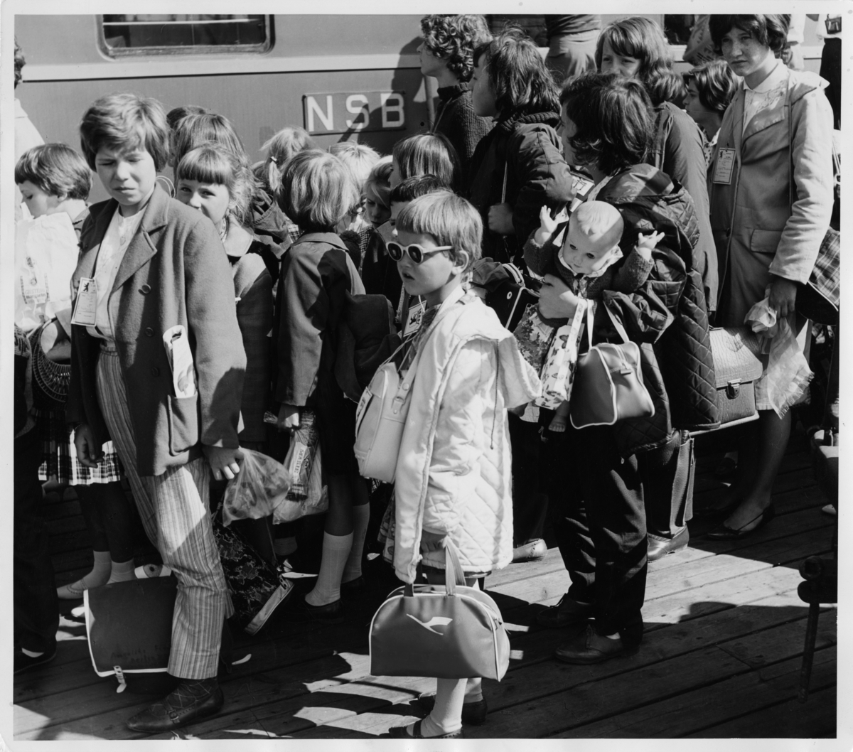 Foto av barn som står på perrongen foran et tog.  Tekst til originalbilde" "Ungdomsaksjonen sendte 350 flyktningebarn fra Oslo Ø." Bildet er stemplet 22. august 1963.