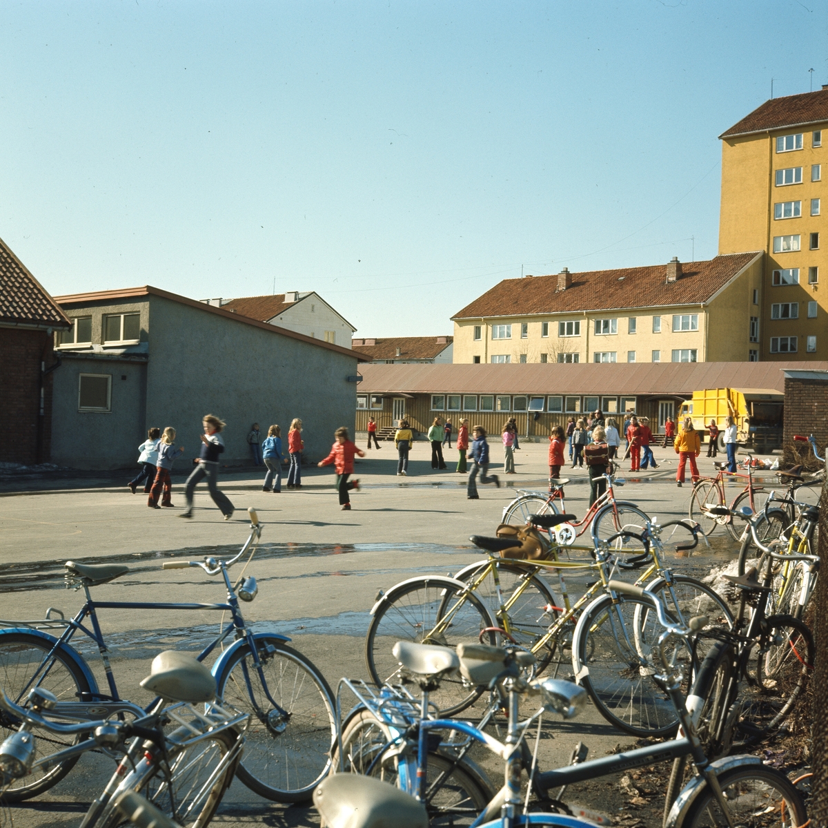 Foto av skoleelever som leker i skolegården ved Årvoll Skole. I forgrunnen en oppsamlingsplass for sykler til elevene.